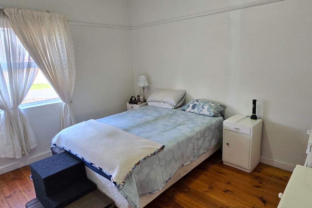 A well-lit bedroom featuring original timber flooring, high ceilings with picture rails, and a large window providing natural light.
