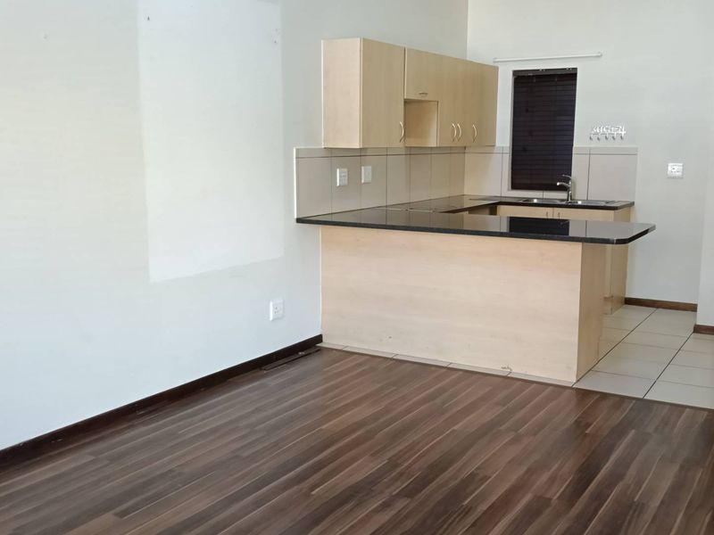 Open plan living area featuring laminate flooring, a compact kitchen with granite countertops, built-in cabinetry, and a tiled backsplash.