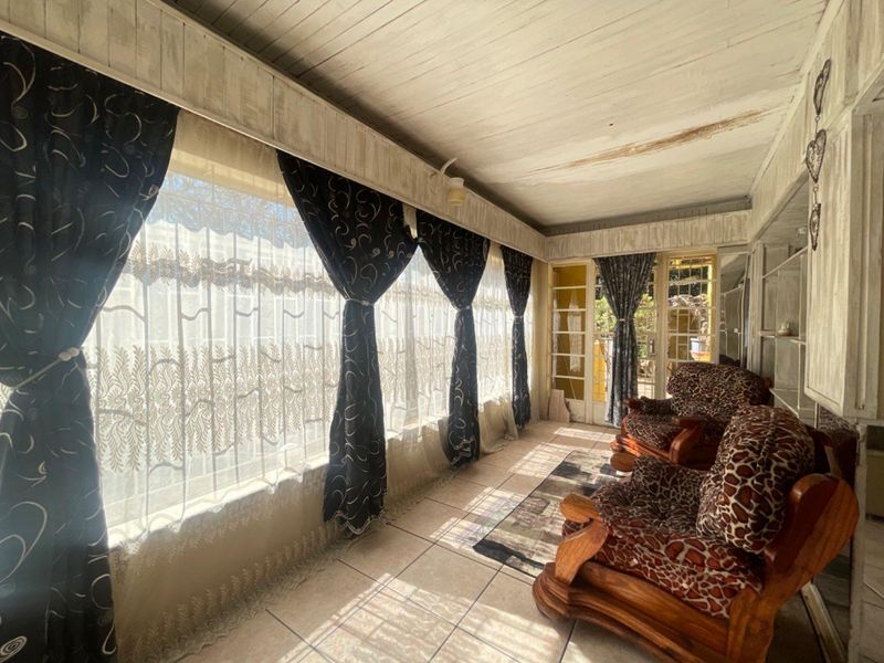 A sunlit enclosed patio or sunroom featuring tiled floors, a timber-paneled ceiling, and large windows providing ample natural light.