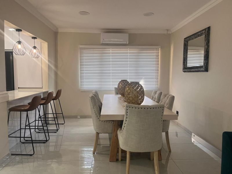 An open-plan dining and kitchen area featuring polished tile flooring, a breakfast bar, and a wall-mounted air conditioning unit.