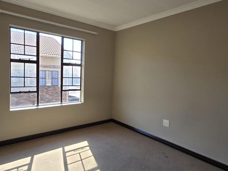 An empty bedroom featuring neutral wall paint, carpeted flooring, and a window with security bars.