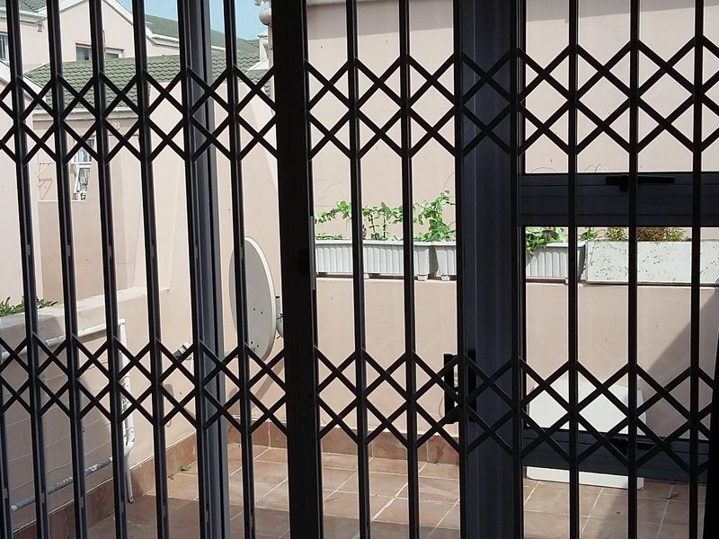 A view from inside looking out through a security gate onto a tiled patio area with exterior walling.