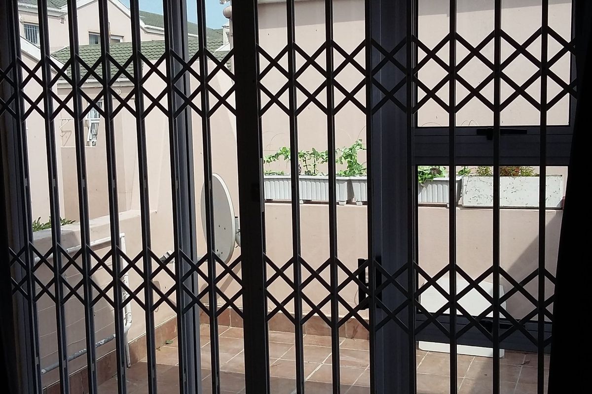 A view from inside looking out through a security gate onto a tiled patio area with exterior walling.