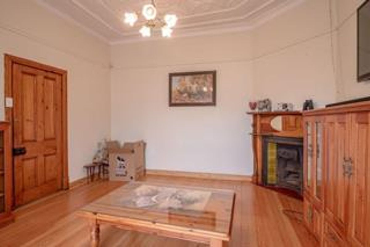 A living room featuring polished timber flooring, an ornate ceiling rose, and a traditional fireplace with a timber mantelpiece.