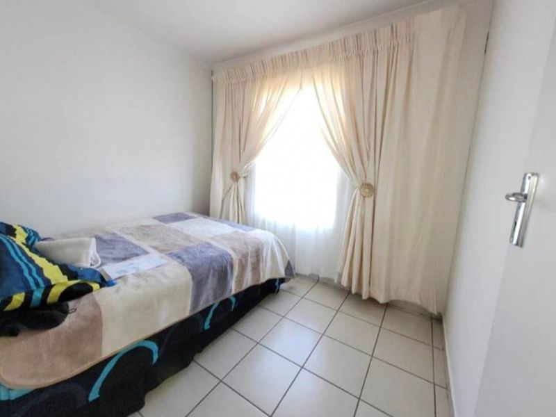 A compact bedroom featuring tiled flooring and a window with installed curtain tracks.
