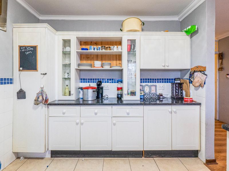 A functional kitchen area featuring white built-in cabinetry, granite countertops, and a blue tiled backsplash, providing ample storage and preparation space.
