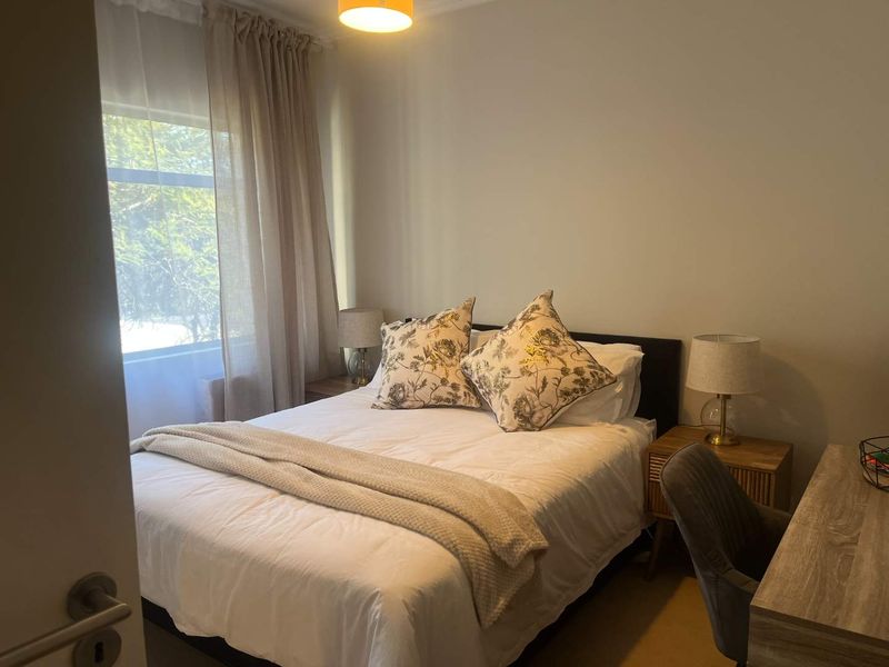 A well-lit bedroom featuring neutral wall tones and a large window, providing a comfortable and functional sleeping space.