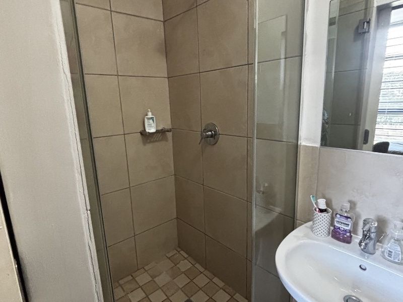 A functional bathroom featuring a tiled shower enclosure with glass door, pedestal basin, and wall-mounted mirror, presenting a standard, lived-in condition.
