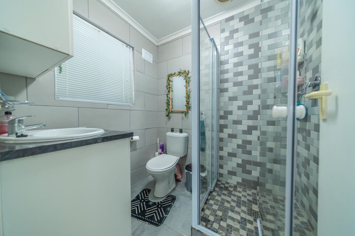 A functional bathroom featuring a vanity with basin, a toilet, and a separate shower enclosure with decorative mosaic wall tiling.