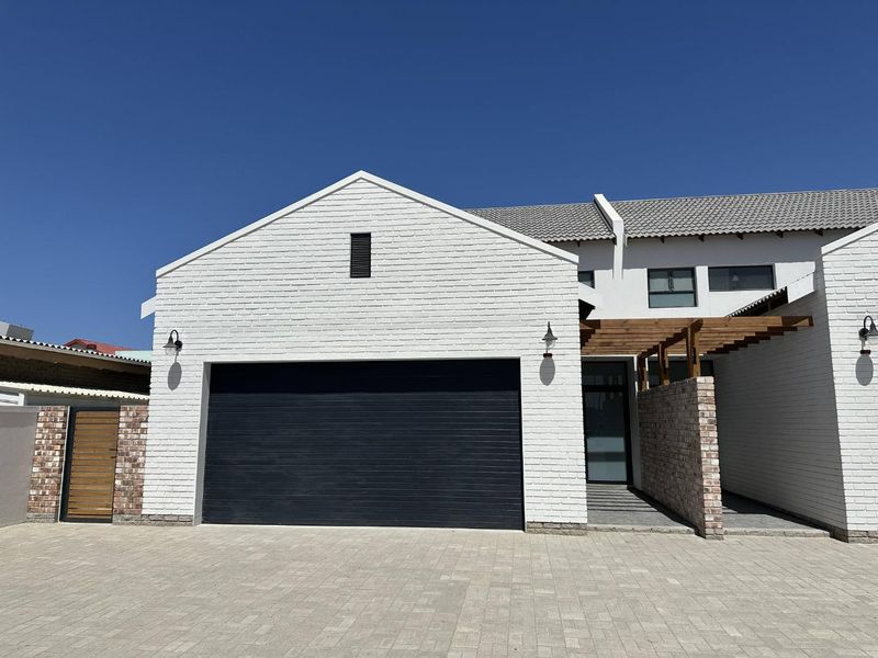 Front elevation of a modern townhouse featuring a white brick facade, dark garage door, timber pergola, and a neat paved driveway.