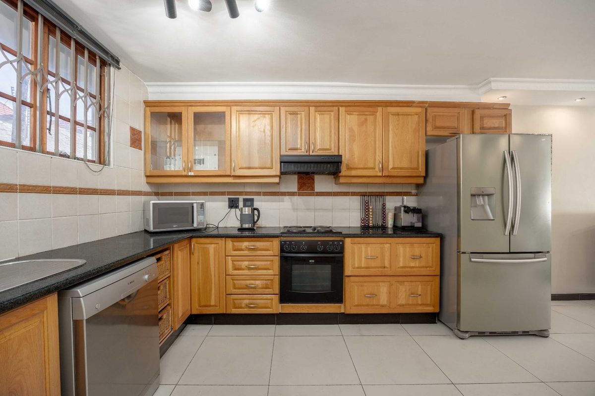 A functional kitchen featuring wooden cabinetry, granite countertops, a built-in oven with hob, and tiled finishes throughout.
