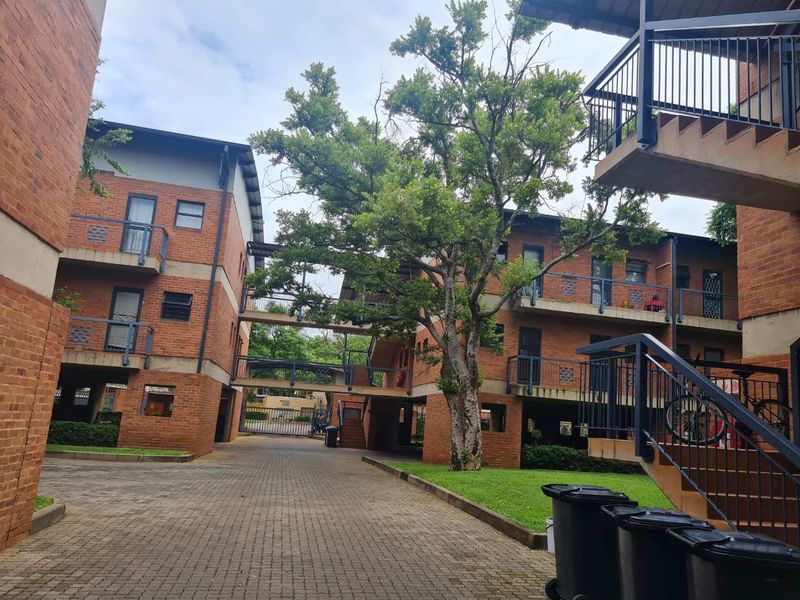 Exterior view of a multi-story apartment complex featuring face brick architecture, paved common areas, metal staircases, and established garden landscaping.