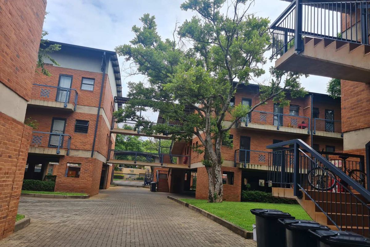 Exterior view of a multi-story apartment complex featuring face brick architecture, paved common areas, metal staircases, and established garden landscaping.