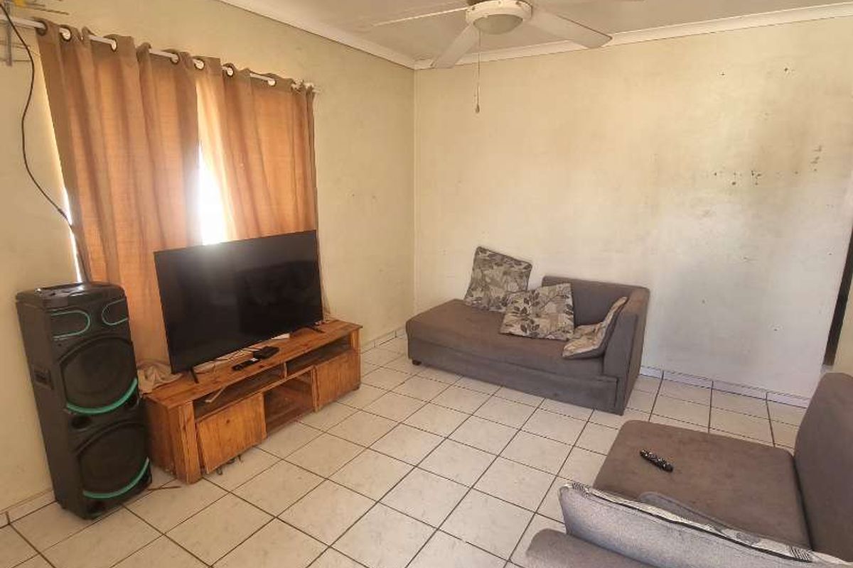 A living room featuring tiled flooring and a ceiling fan, presenting a dated aesthetic with walls in need of cosmetic attention.
