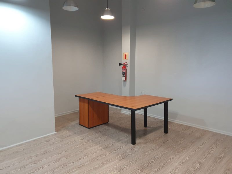 A clean and functional office space featuring light wood-look laminate flooring, neutral walls, and modern overhead lighting.