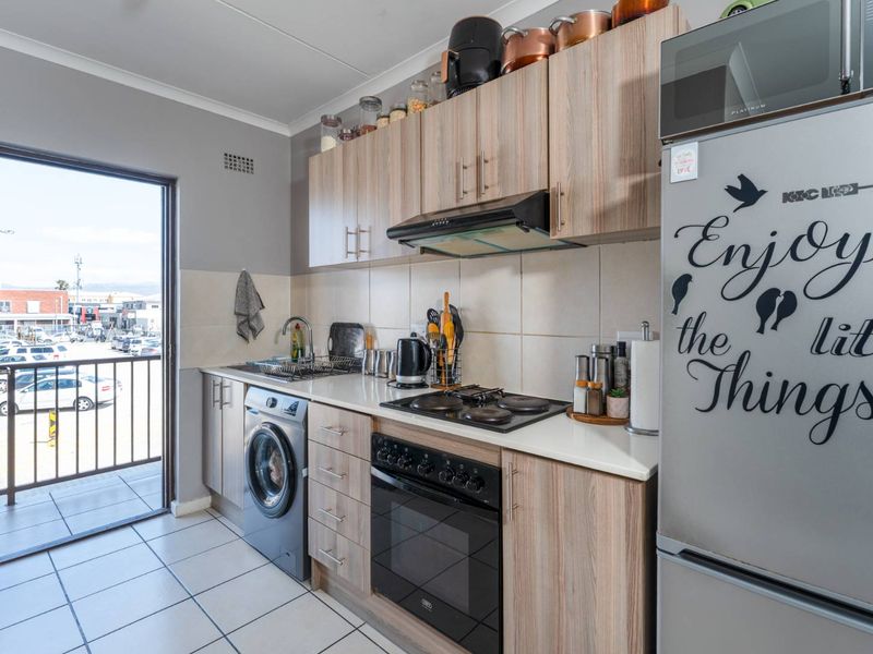 Compact kitchen featuring wood-look cabinetry, built-in oven and hob, tiled backsplash, and direct access to an outdoor balcony area.