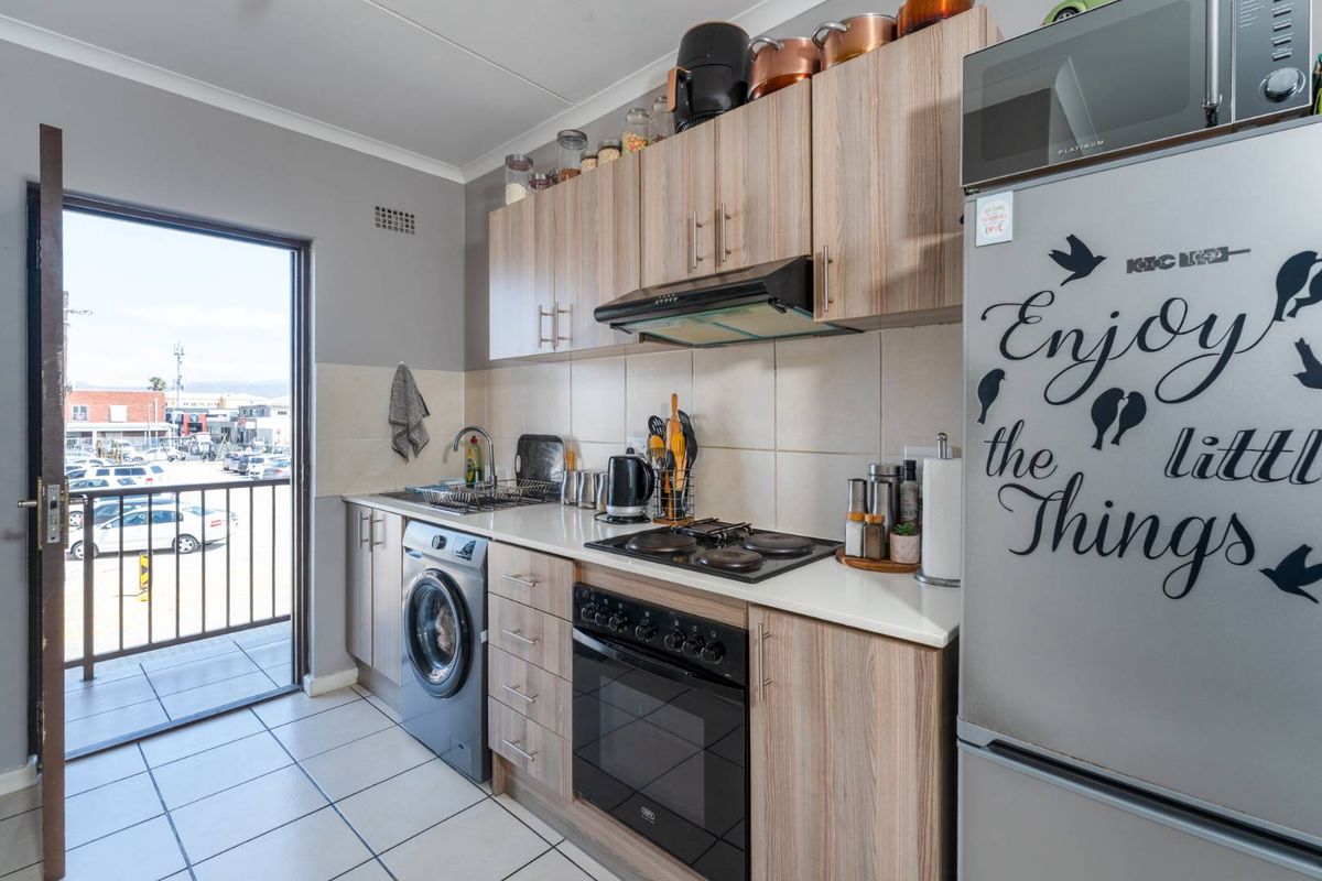 Compact kitchen featuring wood-look cabinetry, built-in oven and hob, tiled backsplash, and direct access to an outdoor balcony area.