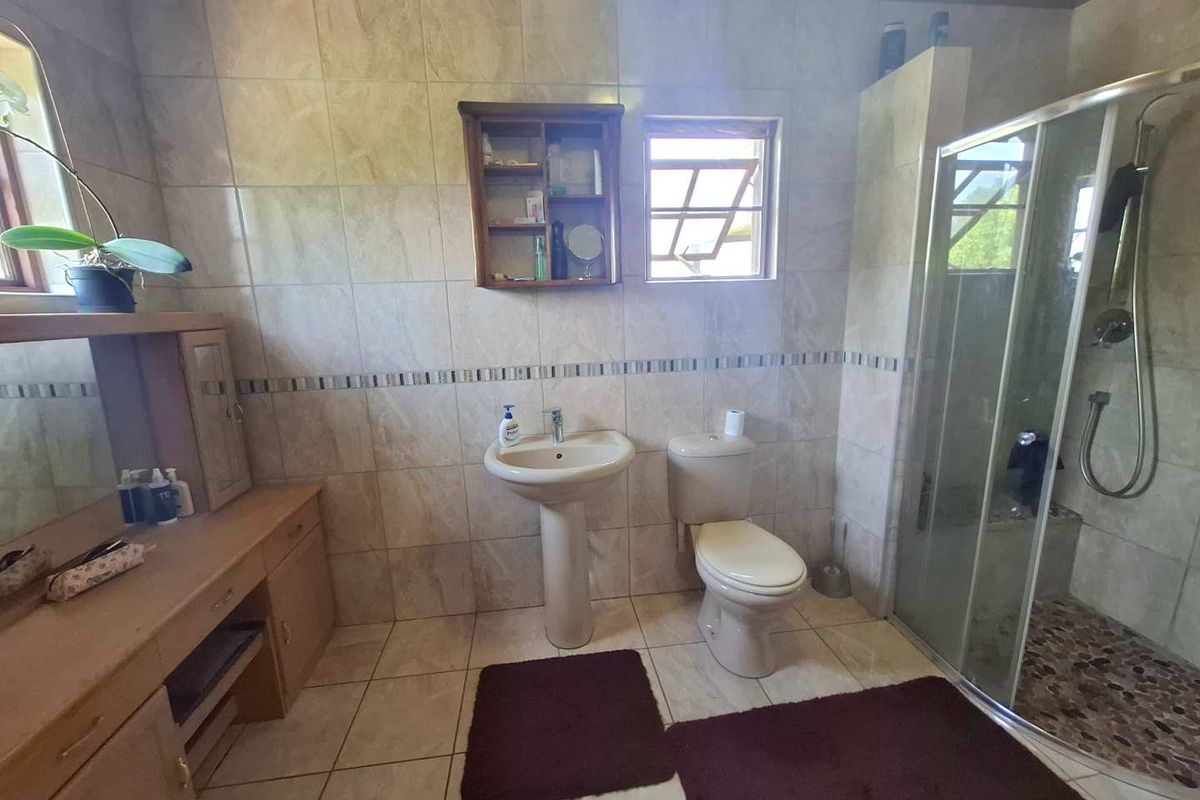 A functional bathroom featuring a pedestal basin, toilet, and a glass-enclosed shower with pebble-style flooring, complemented by neutral wall tiling.