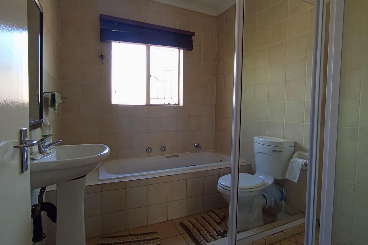 A functional bathroom featuring a built-in bathtub, pedestal basin, and toilet with neutral wall tiling throughout.