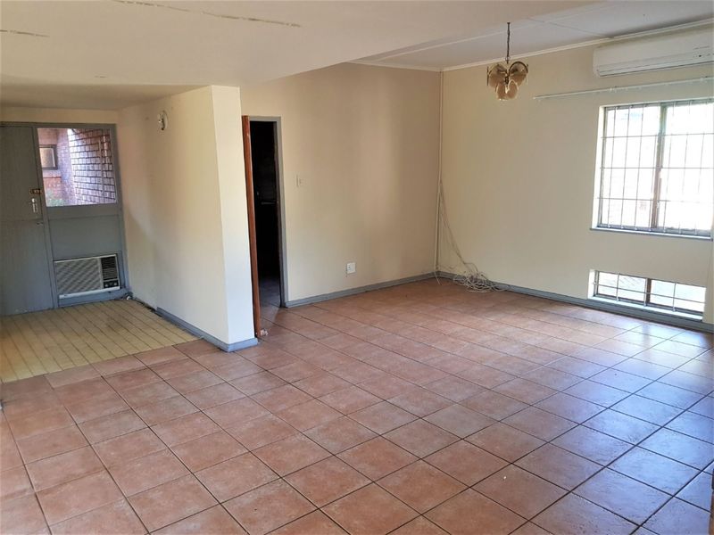 An empty, open-plan living area featuring tiled flooring, security bars on windows, and dual air conditioning units.