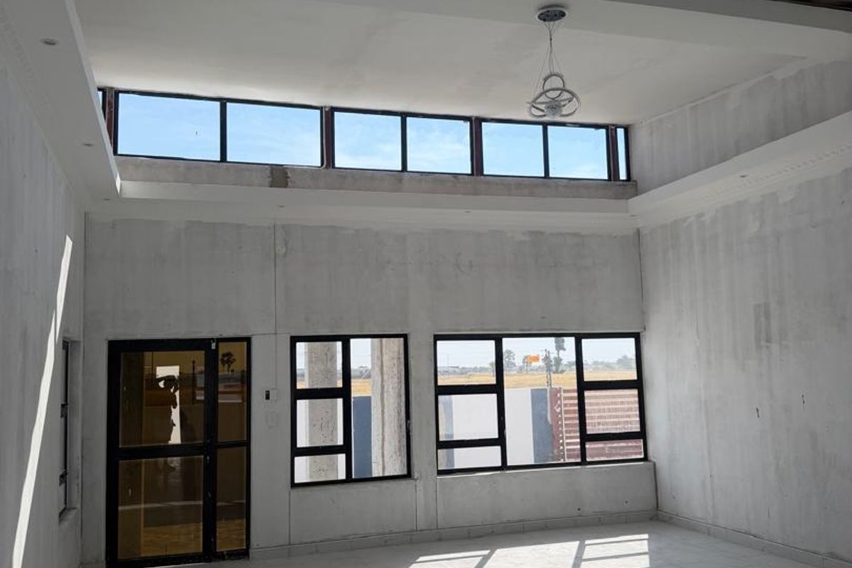 A spacious, unfinished living area featuring high ceilings with clerestory windows, tiled flooring, and large glass-paneled doors leading to the exterior.