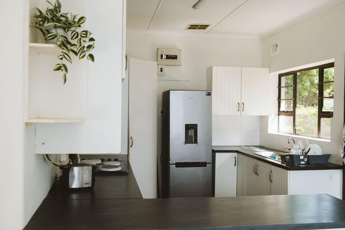A functional kitchen featuring white cabinetry, dark laminate countertops, a built-in hob, and a stainless steel sink with natural light.