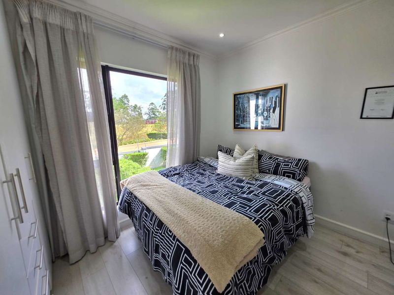 A bright bedroom featuring light laminate flooring, built-in cupboards, and a large sliding glass door that provides natural light and garden views.