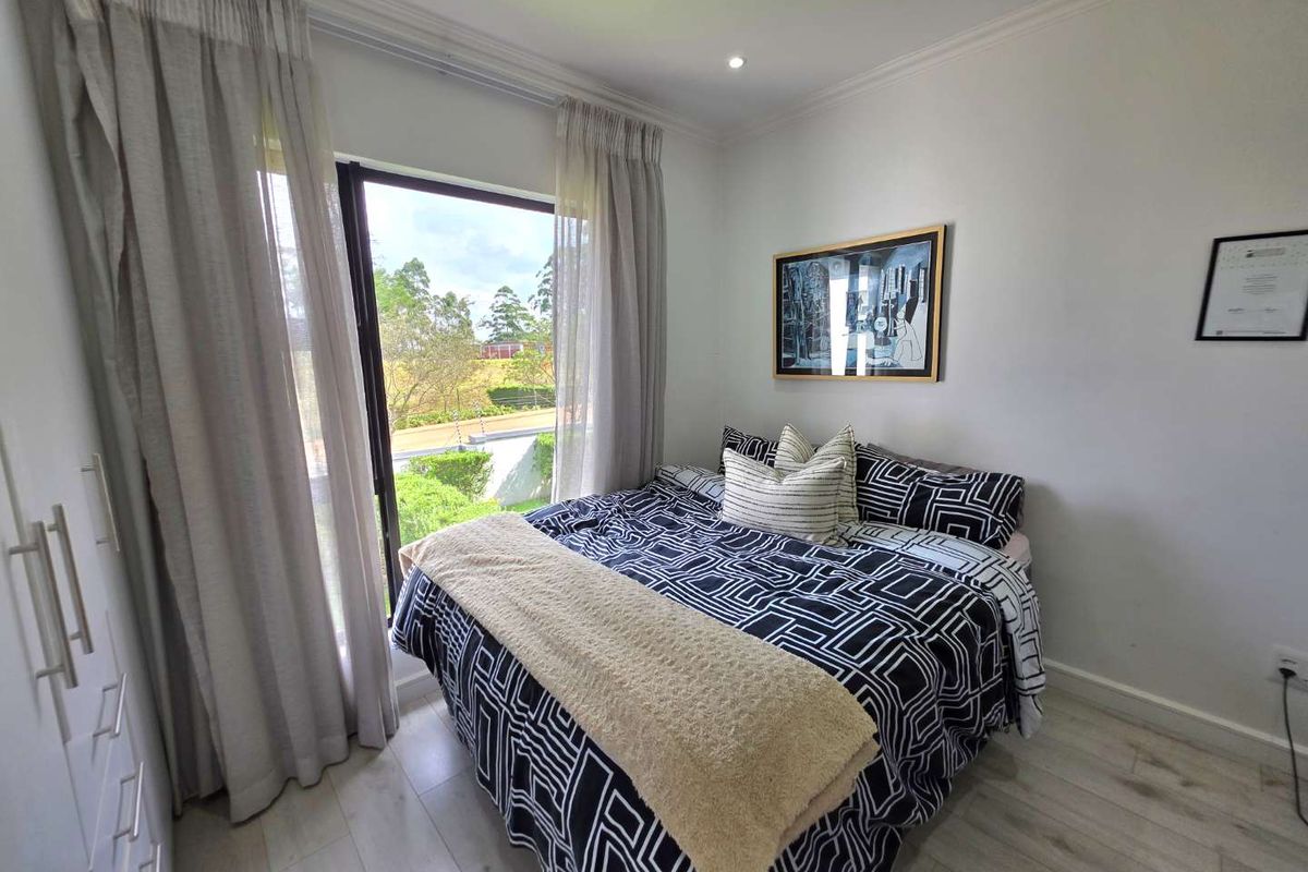 A bright bedroom featuring light laminate flooring, built-in cupboards, and a large sliding glass door that provides natural light and garden views.