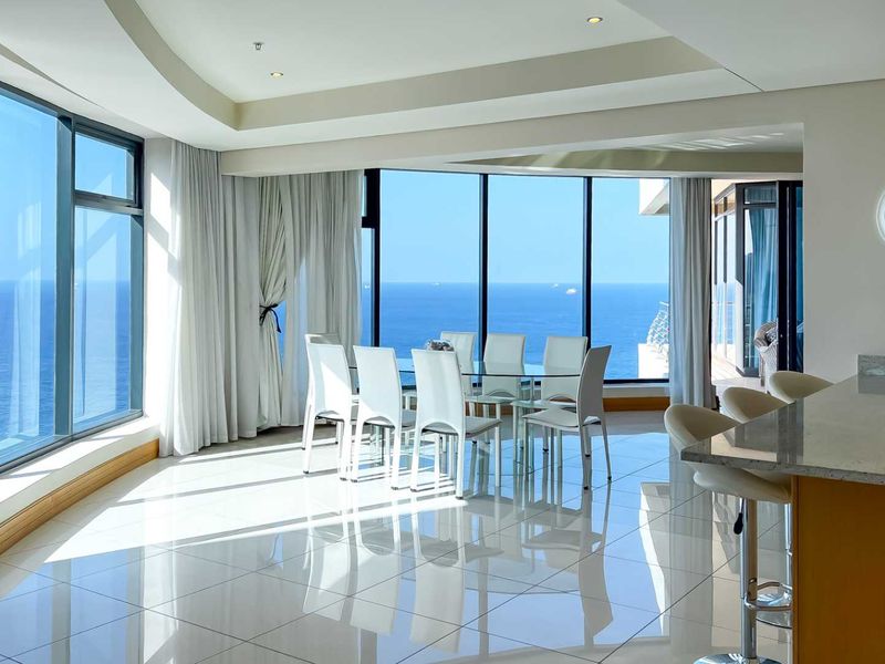 Spacious open-plan living and dining area featuring floor-to-ceiling windows with panoramic ocean views and polished tile flooring.