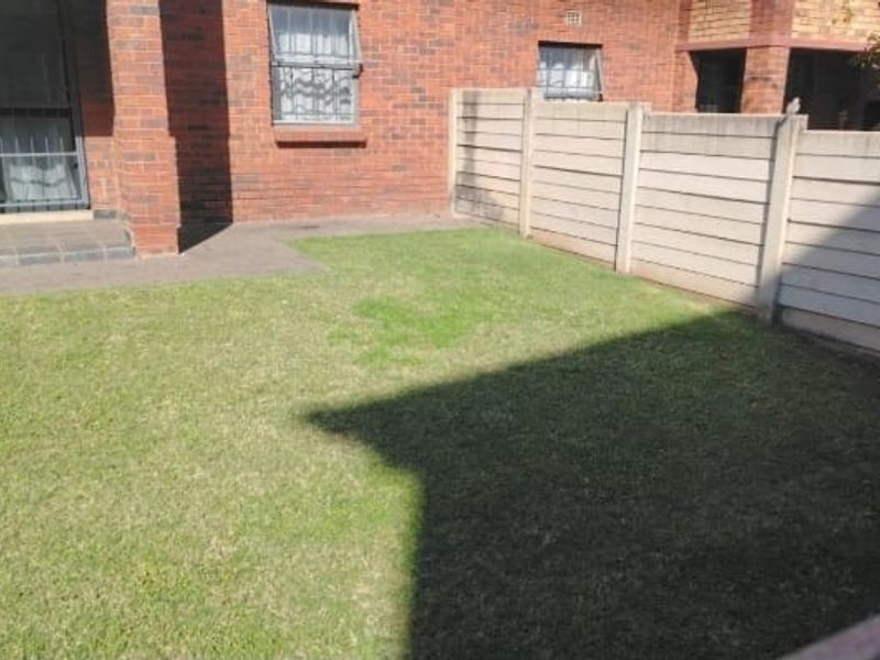 A private rear garden area featuring a small lawn, tiled patio space, and secure brick building facade with boundary walling.