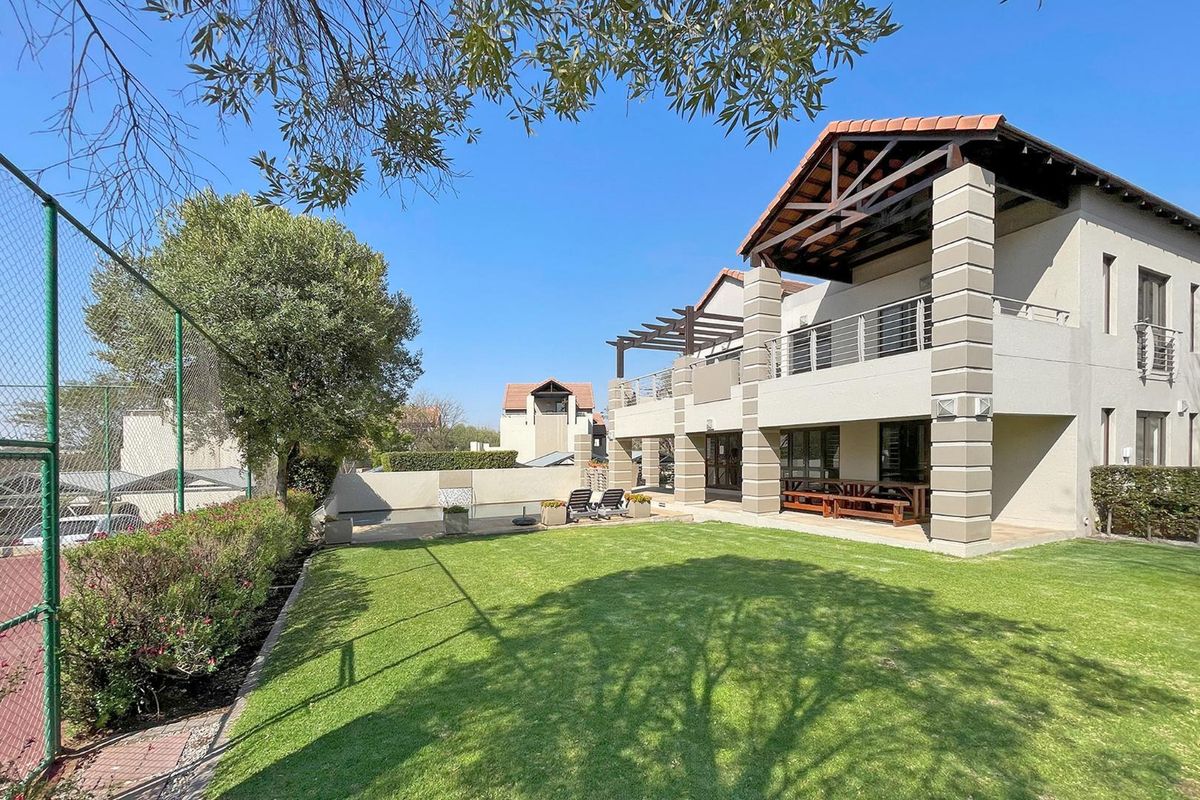 Rear view of the apartment building featuring a well-maintained lawn, covered patio area, and upper-level balcony with metal railings.
