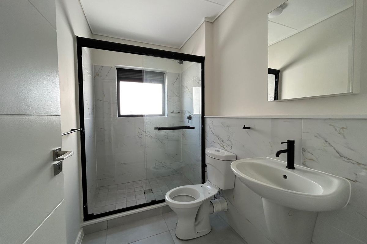 Modern bathroom featuring a walk-in shower with black frame, pedestal basin with matte black tap, and marble-look wall tiling.