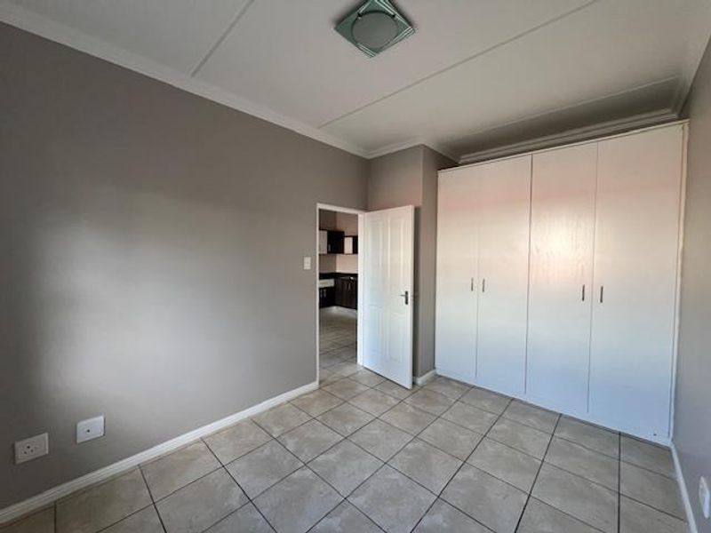 A clean, empty bedroom featuring neutral grey walls, tiled flooring, and ample built-in cupboard storage space.