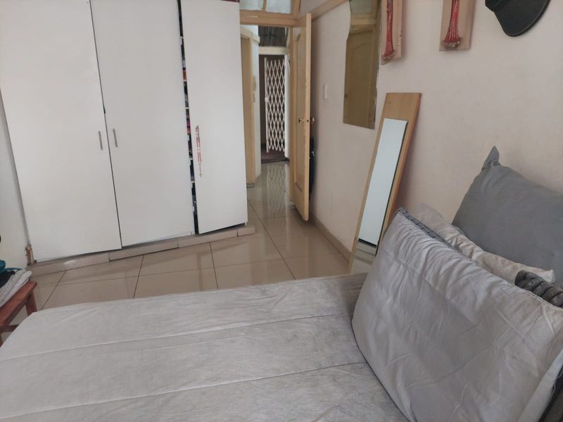 A bedroom featuring tiled flooring and built-in cupboards, with a view leading into a hallway with a security gate.