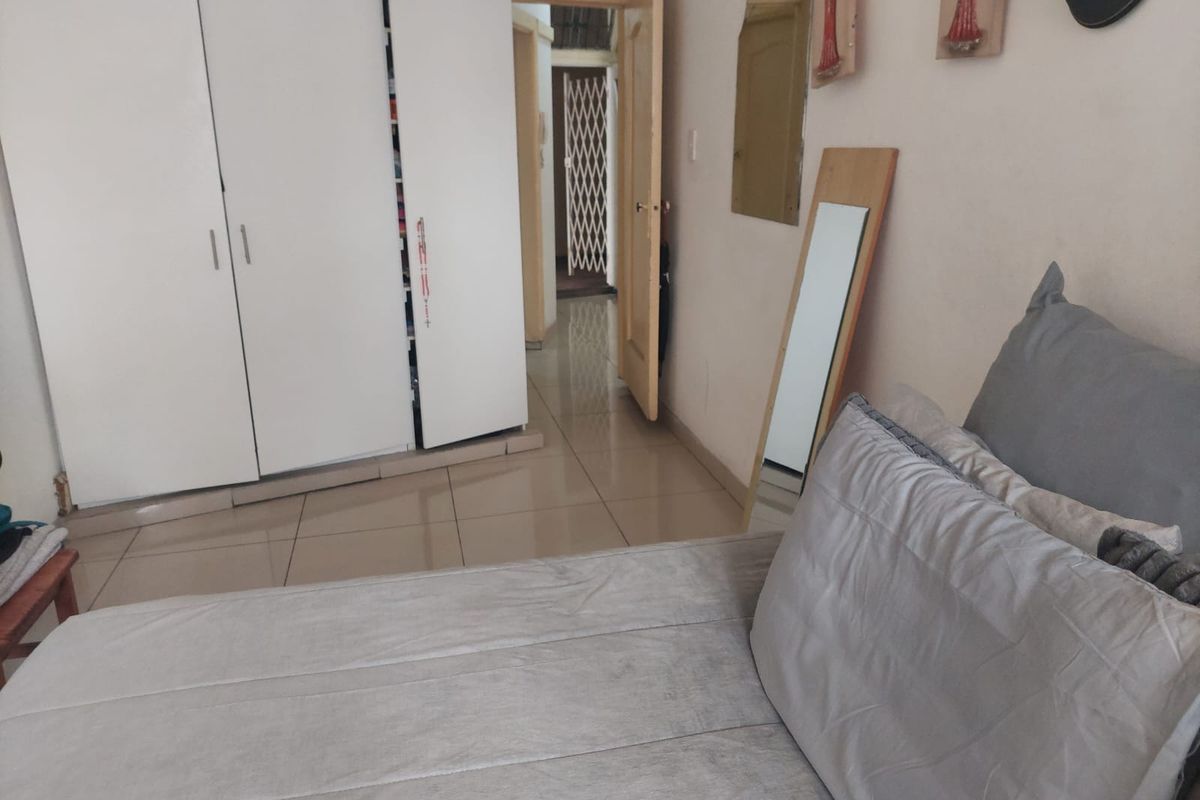 A bedroom featuring tiled flooring and built-in cupboards, with a view leading into a hallway with a security gate.