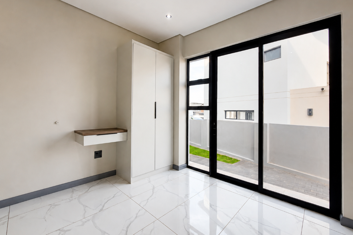 Modern bedroom featuring sleek white built-in cabinetry, a floating desk, polished marble-look tile flooring, and large sliding glass doors opening to an outdoor area.