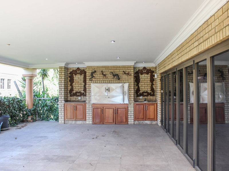 Covered patio featuring a built-in braai, wooden cabinetry, tiled flooring, and large stacking glass doors providing seamless indoor-outdoor flow.