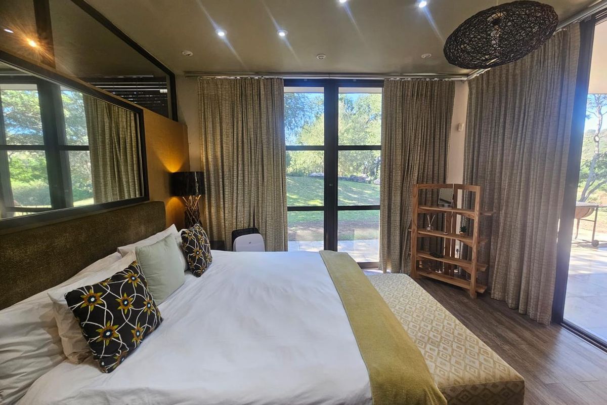 Spacious bedroom featuring large floor-to-ceiling windows with garden views, recessed ceiling lighting, and direct access to an outdoor patio area.
