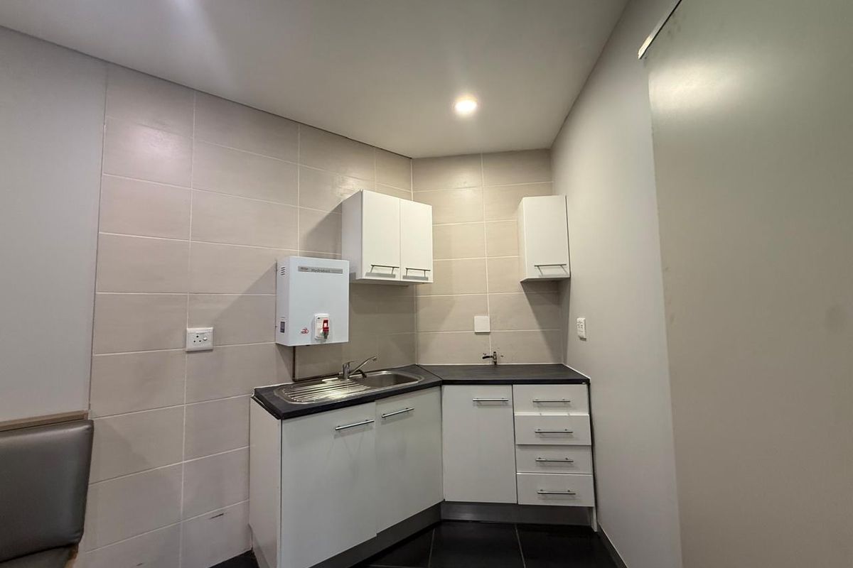 A compact office kitchenette featuring built-in cabinetry, a stainless steel sink, and a wall-mounted water heater.