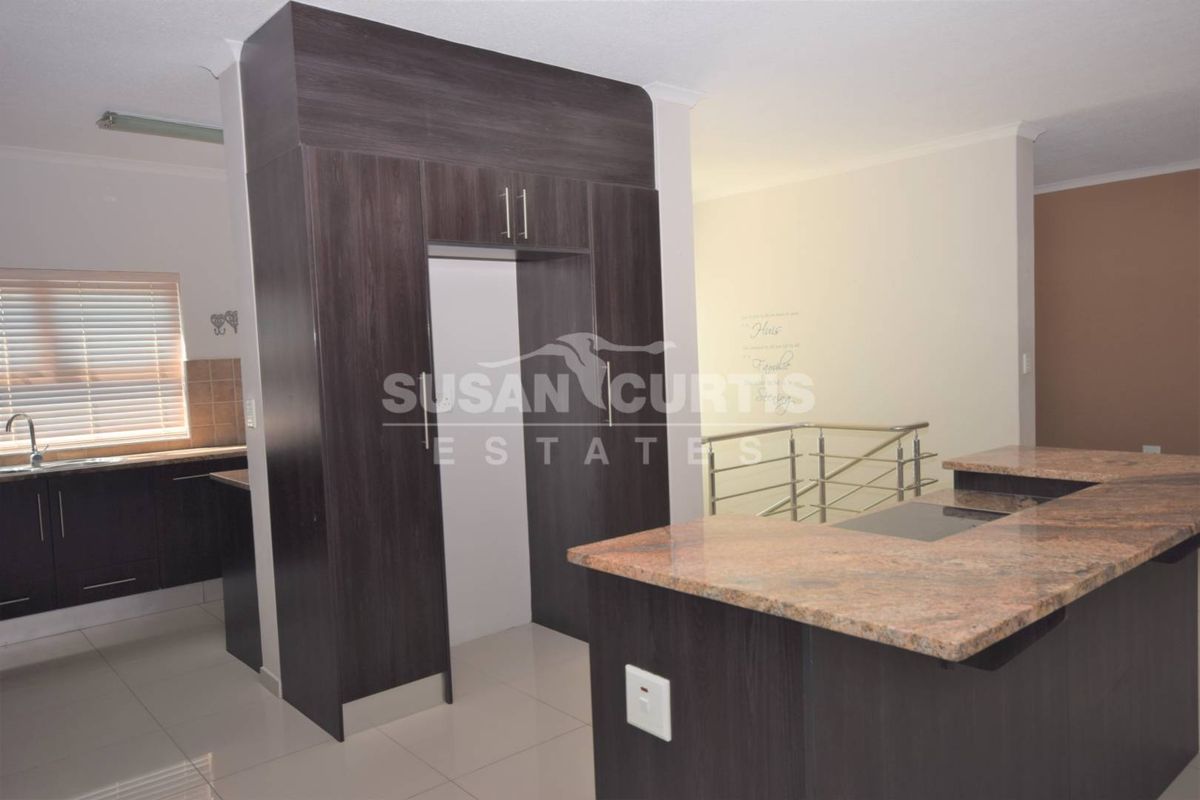 Modern kitchen featuring dark wood cabinetry, granite countertops, a breakfast bar with integrated hob, and tiled flooring in an open-plan layout.