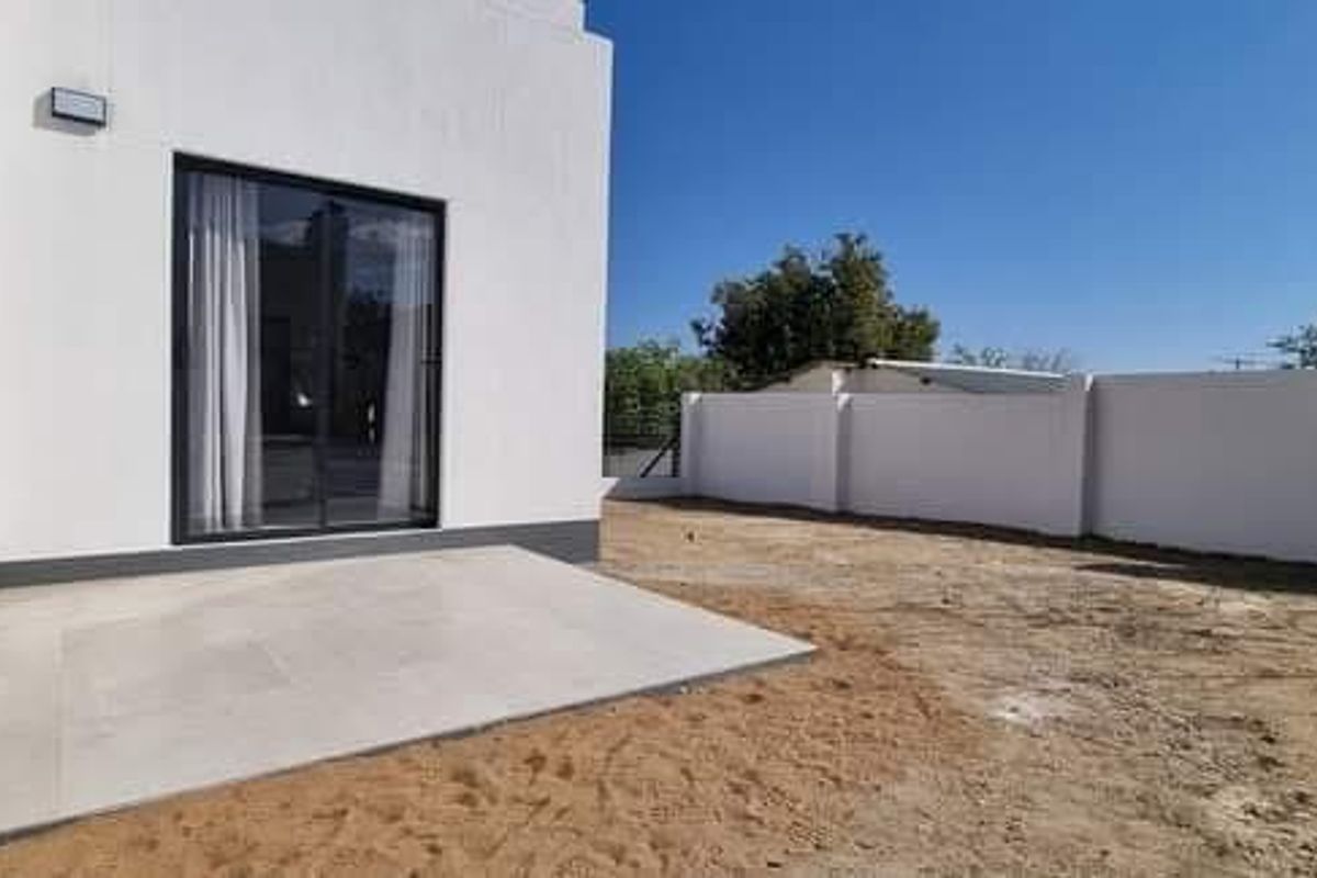 Rear view of the property featuring a paved patio area, sliding glass doors, and a large, unlandscaped garden space enclosed by a perimeter wall.