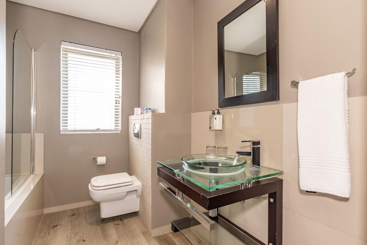 Modern bathroom featuring a glass vessel sink, wall-mounted toilet, and a glass-enclosed shower with neutral wall finishes.