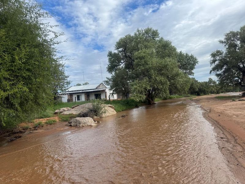 A view of the farm property featuring a building with a corrugated metal roof situated near a flowing stream and natural landscape.