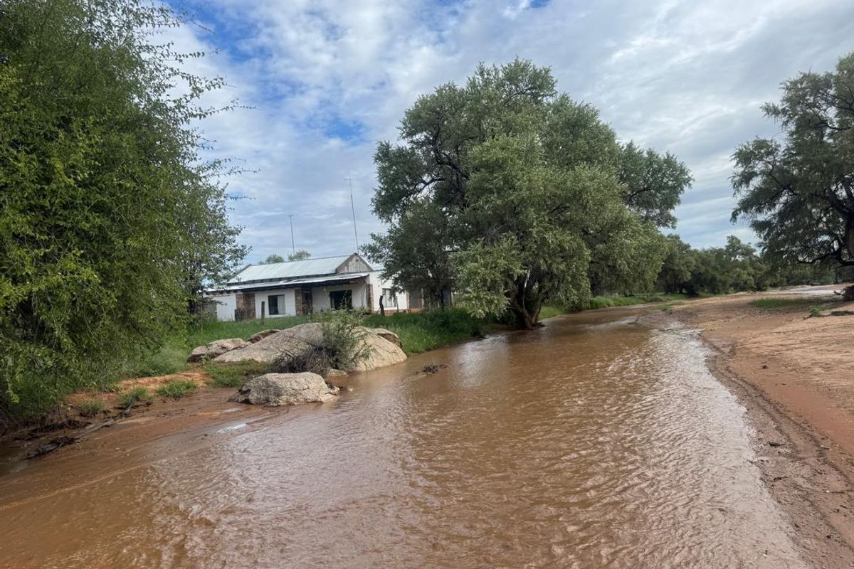 A view of the farm property featuring a building with a corrugated metal roof situated near a flowing stream and natural landscape.