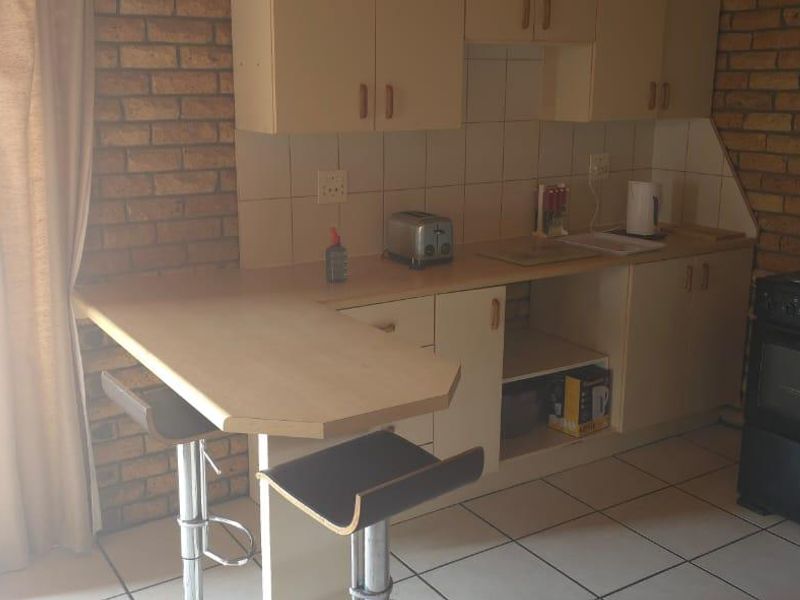 Compact kitchen featuring built-in cabinetry, a tiled backsplash, a breakfast bar, and a freestanding stove, with direct access to an outdoor area.