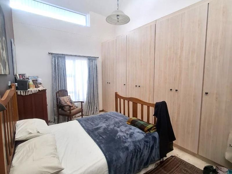 A well-lit bedroom featuring extensive built-in cupboards, high ceilings with a clerestory window, and a central pendant light fixture.