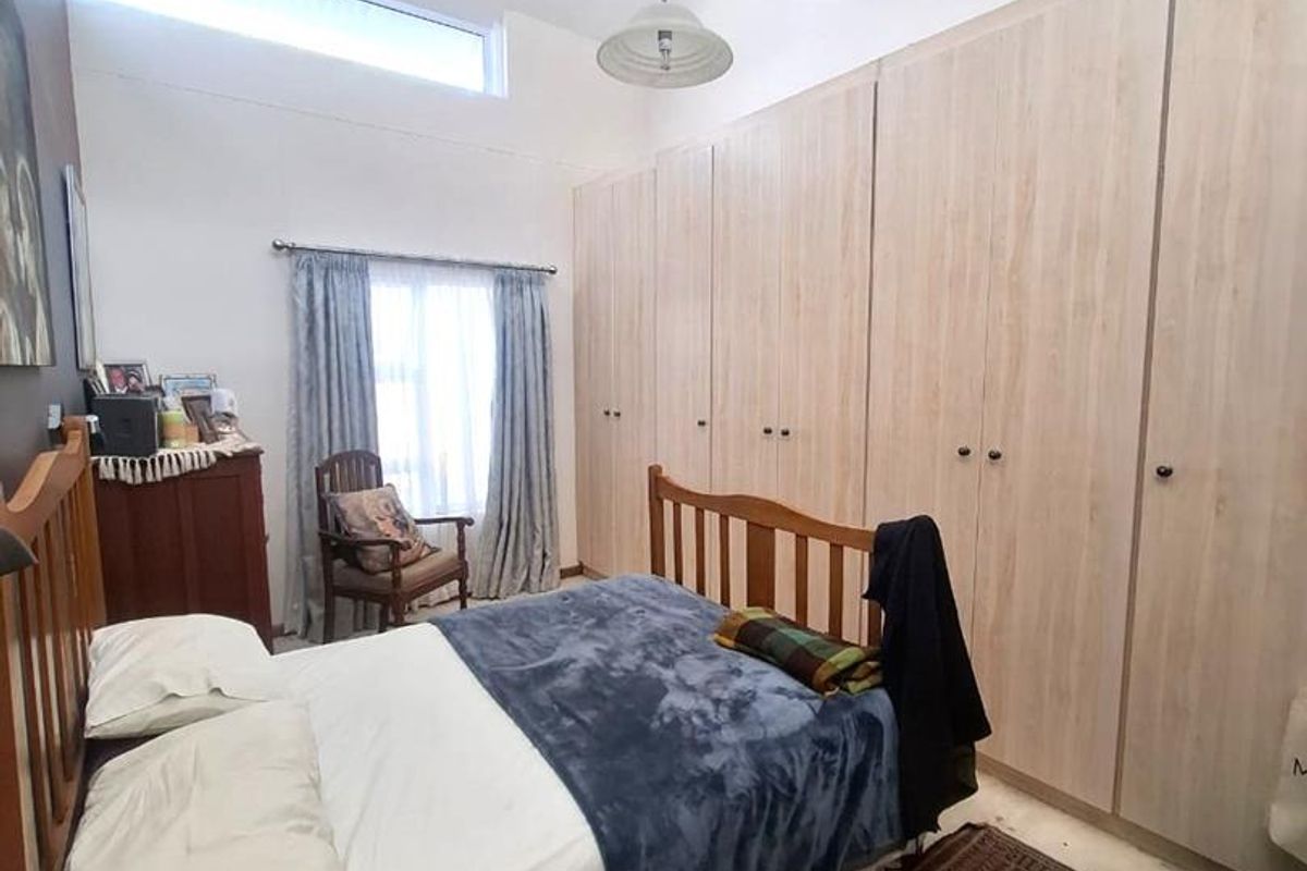 A well-lit bedroom featuring extensive built-in cupboards, high ceilings with a clerestory window, and a central pendant light fixture.