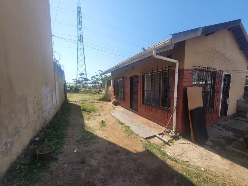 Rear exterior view of the cottage featuring brick and plaster facade, security bars on windows, and a paved walkway along the side of the building.