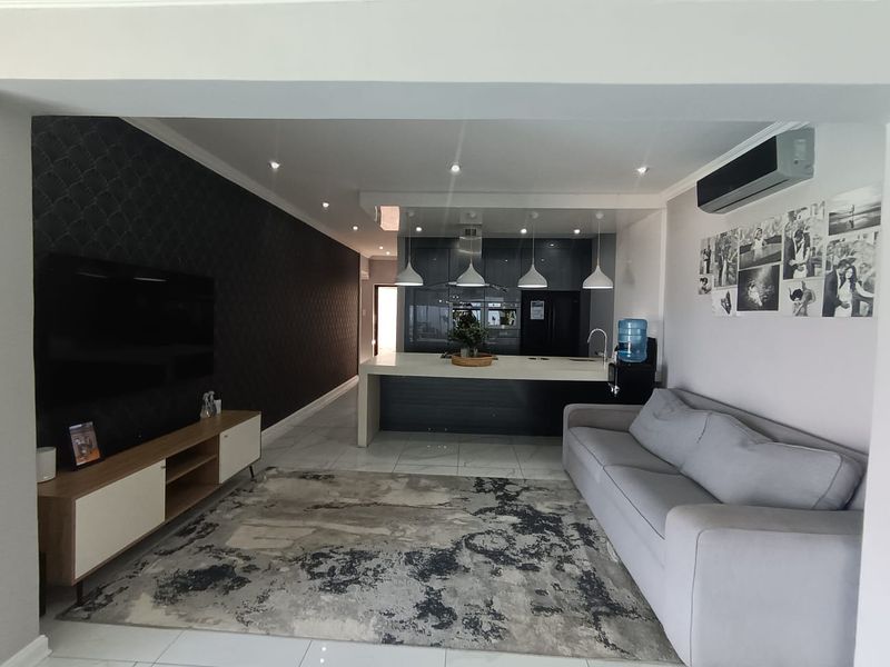 Modern open-plan living area featuring a sleek kitchen island, contemporary cabinetry, recessed lighting, and tiled flooring, creating a cohesive and functional living space.