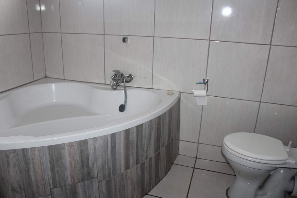 A functional bathroom featuring a corner bathtub with wood-look tiling and a standard toilet, finished with neutral wall tiles.
